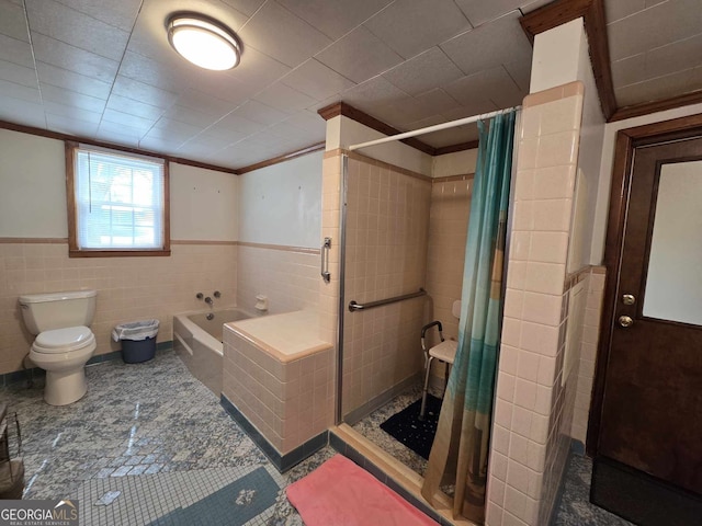 bathroom with a bath, wainscoting, a shower stall, and tile walls