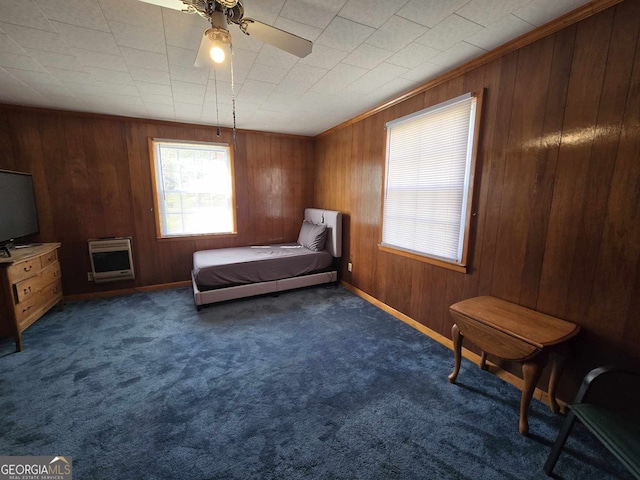 bedroom with ceiling fan, dark colored carpet, wood walls, and heating unit