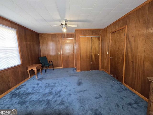 sitting room with ornamental molding, carpet, a ceiling fan, and wooden walls