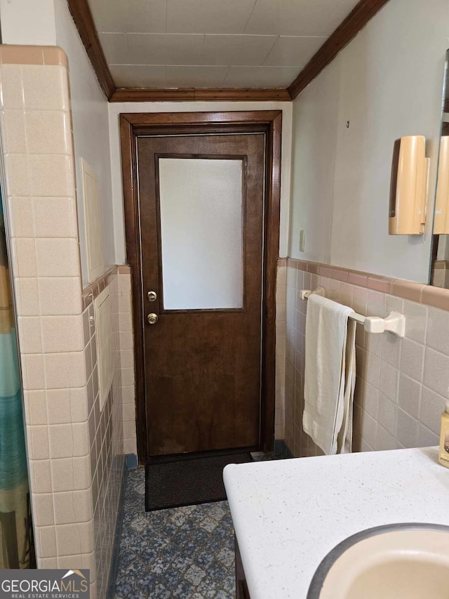 bathroom featuring a wainscoted wall, ornamental molding, and tile walls