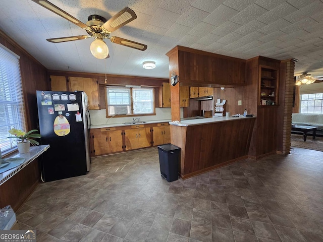 kitchen featuring freestanding refrigerator, a healthy amount of sunlight, light countertops, and wooden walls