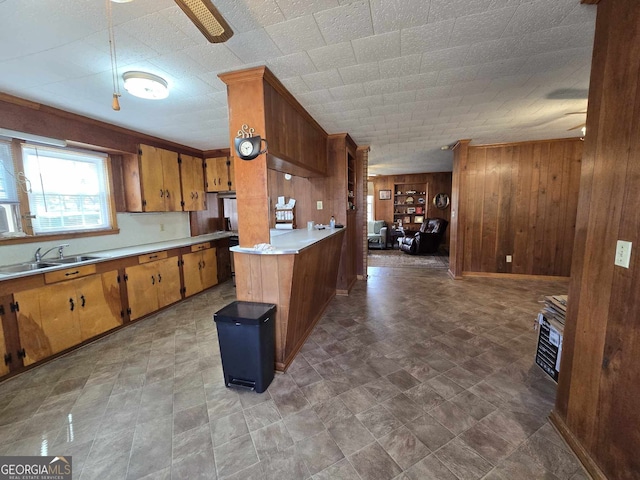 kitchen with light countertops, brown cabinets, a sink, and wooden walls