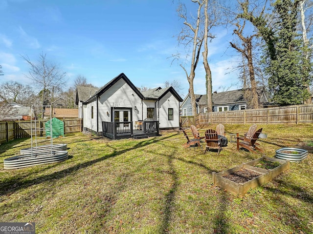 back of property with a deck, a fenced backyard, a yard, and a fire pit