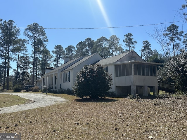 view of side of property featuring driveway, a sunroom, and a chimney