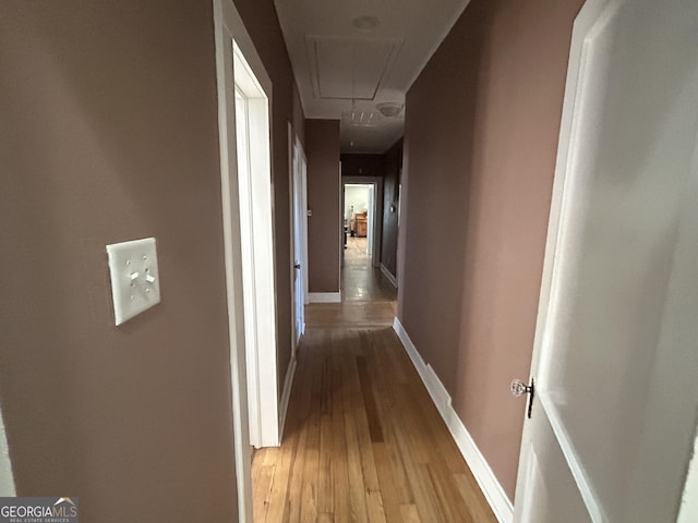 hall featuring light wood finished floors, attic access, and baseboards