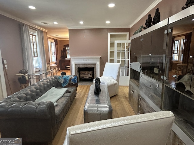 living area featuring a wealth of natural light, light wood-type flooring, crown molding, and a premium fireplace