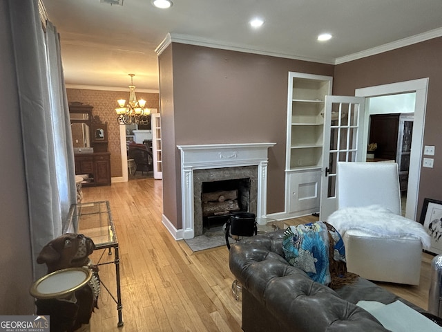 living area featuring crown molding, light wood finished floors, a premium fireplace, baseboards, and a chandelier