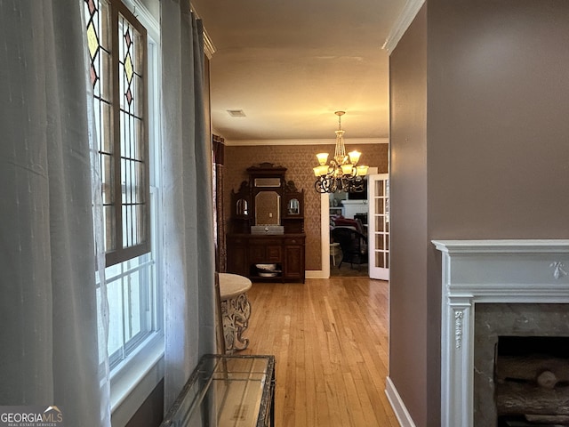 hallway with baseboards, light wood-style flooring, ornamental molding, a notable chandelier, and a wealth of natural light