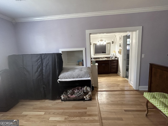 bedroom with crown molding, light wood-style floors, baseboards, and a sink