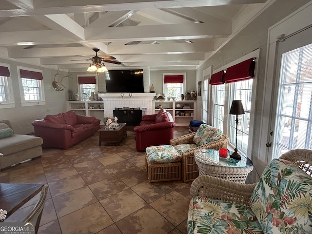 living area with beam ceiling, plenty of natural light, a brick fireplace, and a ceiling fan