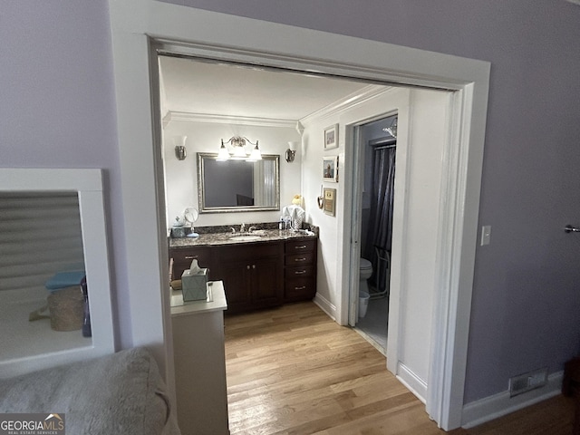 bathroom with vanity, wood finished floors, baseboards, crown molding, and toilet