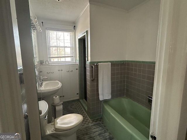 bathroom featuring a garden tub, a wainscoted wall, a sink, a textured ceiling, and tile walls