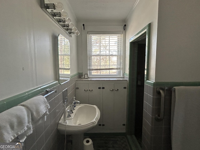 bathroom with wainscoting, tile walls, crown molding, and a sink