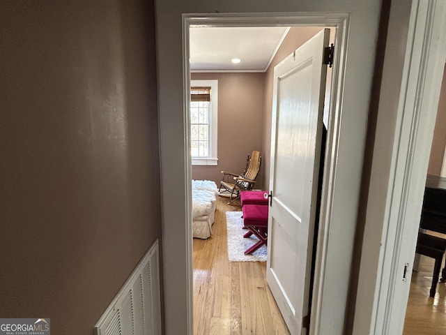 hallway with visible vents, crown molding, and light wood finished floors