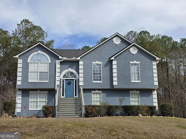 split foyer home featuring stucco siding and a front lawn