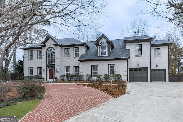 view of front of house with roof with shingles, an attached garage, fence, decorative driveway, and brick siding