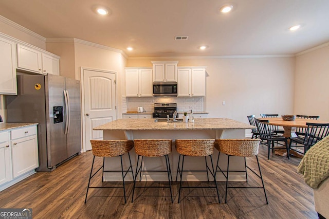 kitchen with appliances with stainless steel finishes, white cabinetry, a center island with sink, and backsplash