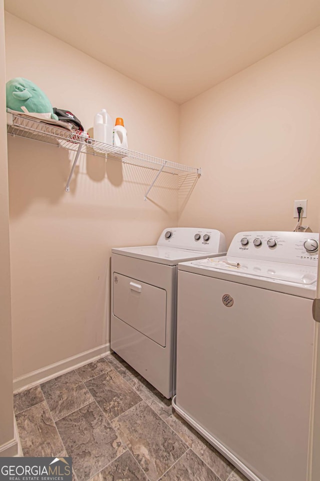 clothes washing area with laundry area, stone finish flooring, washer and clothes dryer, and baseboards