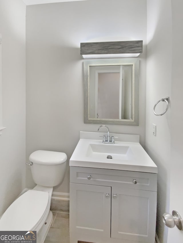 half bath featuring vanity, toilet, and baseboards