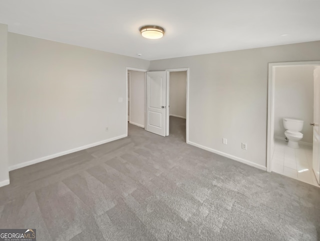 unfurnished bedroom featuring ensuite bath, carpet flooring, and baseboards