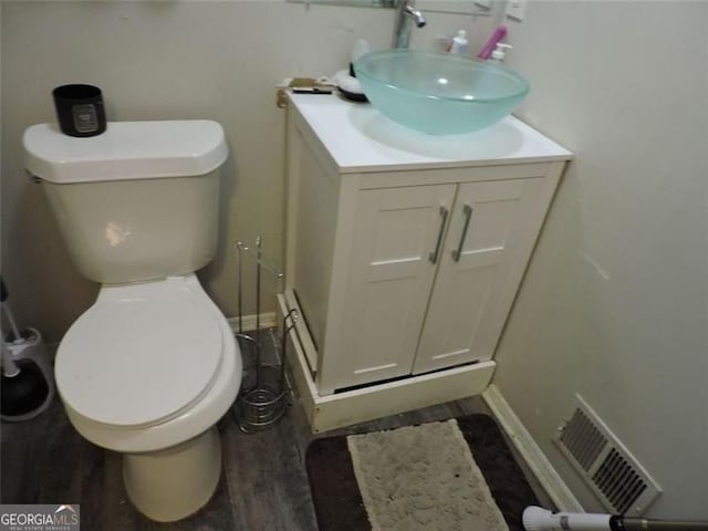 bathroom with toilet, wood finished floors, vanity, visible vents, and baseboards