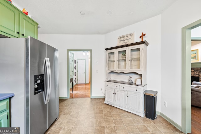 kitchen with glass insert cabinets, stainless steel fridge, baseboards, and green cabinets