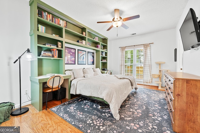 bedroom with visible vents, a textured ceiling, ceiling fan, and wood finished floors