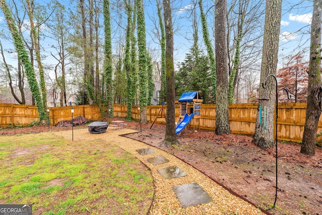 view of yard featuring a playground, a fenced backyard, and a fire pit