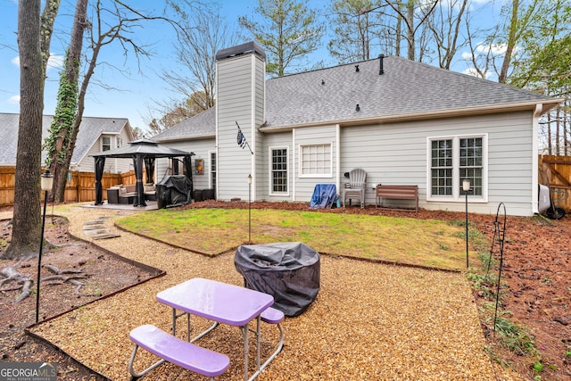 rear view of house with roof with shingles, a fenced backyard, a chimney, a gazebo, and a patio area