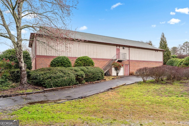 exterior space with a yard, driveway, brick siding, and stairs