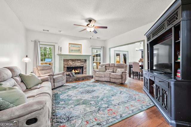 living room with visible vents, ceiling fan with notable chandelier, a fireplace, wood finished floors, and a textured ceiling