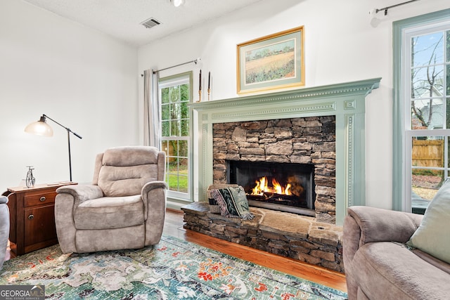 living area with visible vents, a fireplace, a textured ceiling, and wood finished floors