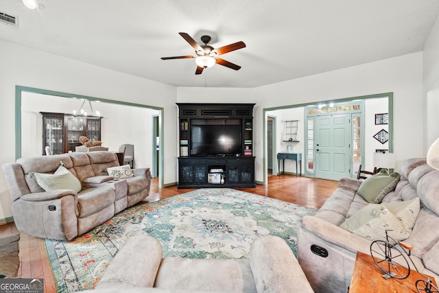 living room with visible vents, wood finished floors, and ceiling fan with notable chandelier