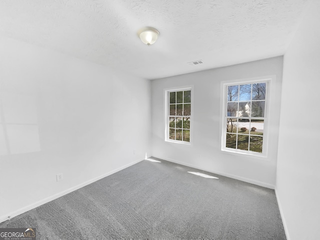 empty room featuring carpet flooring, visible vents, baseboards, and a textured ceiling