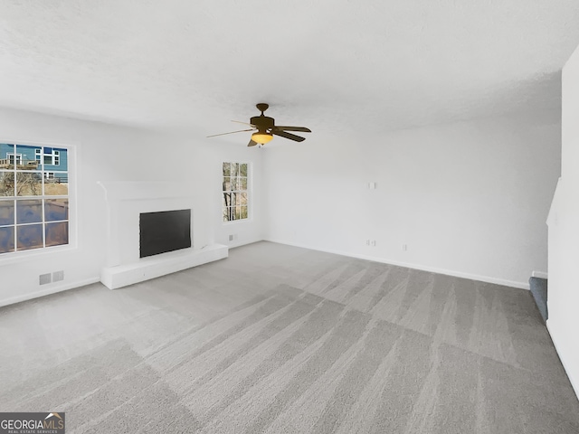 unfurnished living room with visible vents, a fireplace with raised hearth, baseboards, ceiling fan, and carpet flooring