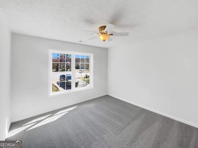 empty room with visible vents, baseboards, ceiling fan, dark carpet, and a textured ceiling