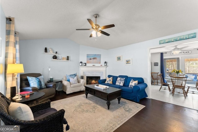 living area with ceiling fan, lofted ceiling, a textured ceiling, dark wood-style flooring, and a fireplace