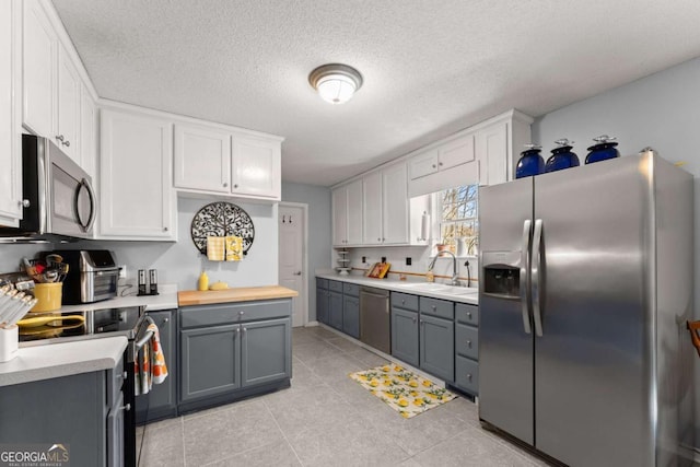 kitchen featuring stainless steel appliances, white cabinets, a sink, and gray cabinetry