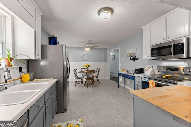 kitchen featuring appliances with stainless steel finishes, white cabinets, wainscoting, a sink, and ceiling fan