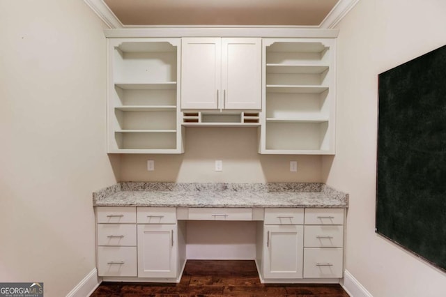 unfurnished office featuring dark wood-style floors, ornamental molding, built in desk, and baseboards