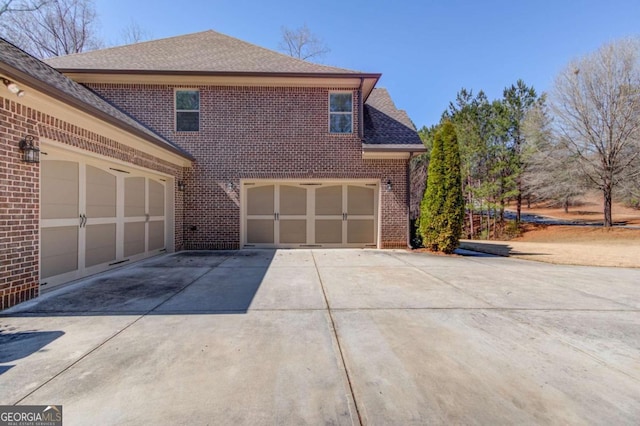 view of side of home featuring a garage, a shingled roof, concrete driveway, and brick siding