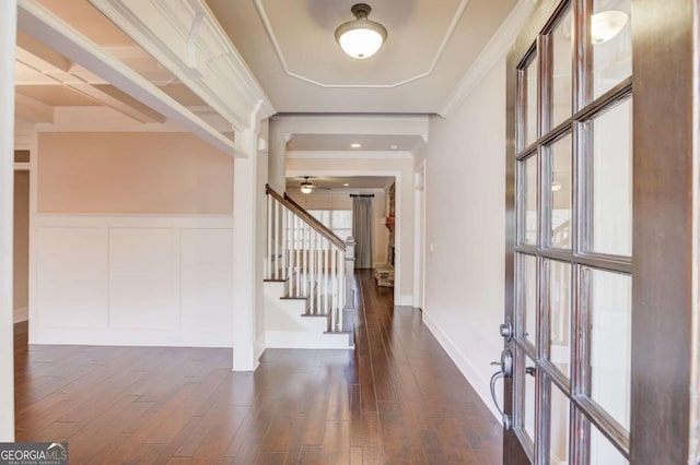 entryway featuring dark wood-style floors, a decorative wall, ornamental molding, wainscoting, and stairs