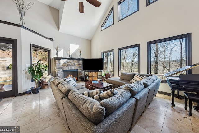 living room featuring light tile patterned floors, a towering ceiling, a ceiling fan, a stone fireplace, and baseboards