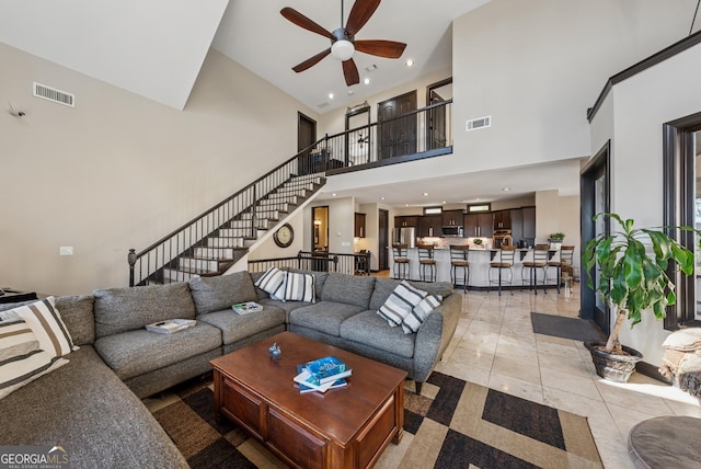 living room with stairs, a ceiling fan, visible vents, and light tile patterned flooring