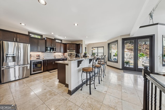 kitchen featuring backsplash, appliances with stainless steel finishes, dark brown cabinetry, light stone countertops, and a kitchen breakfast bar