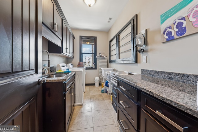 kitchen featuring visible vents, washer and clothes dryer, dark brown cabinets, a sink, and light tile patterned flooring