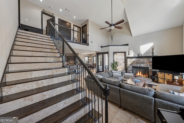 living room with stairs, ceiling fan, a stone fireplace, and tile patterned flooring