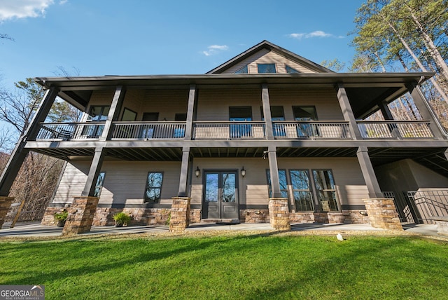 back of property featuring stone siding, a yard, and a balcony