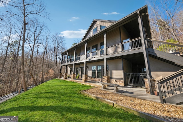 back of property with stone siding, a yard, and a balcony