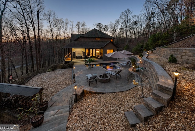 back of house at dusk featuring a patio and a fire pit